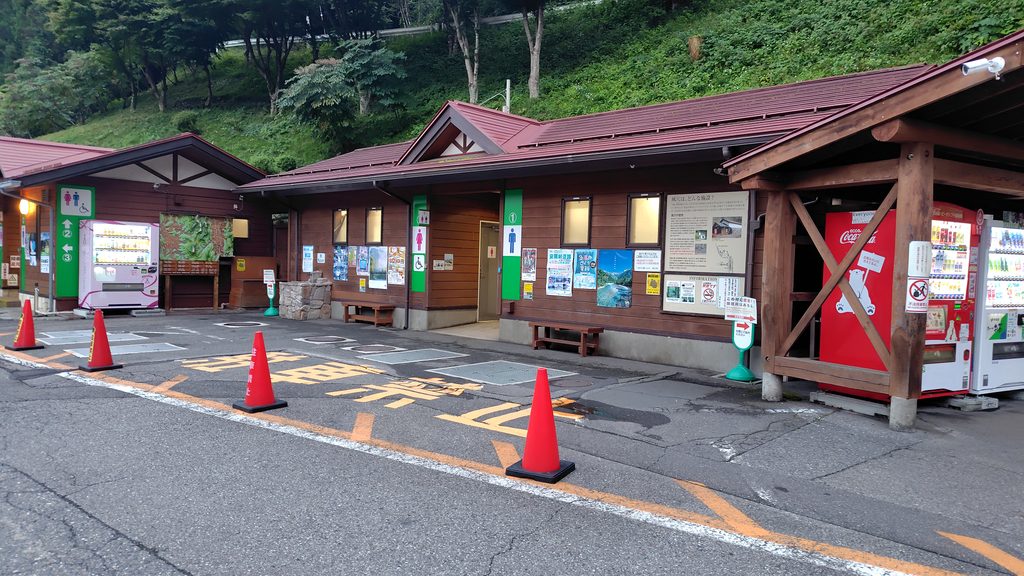 道の駅 風穴の里のトイレ①外観。木造の建物と自動販売機が並ぶ