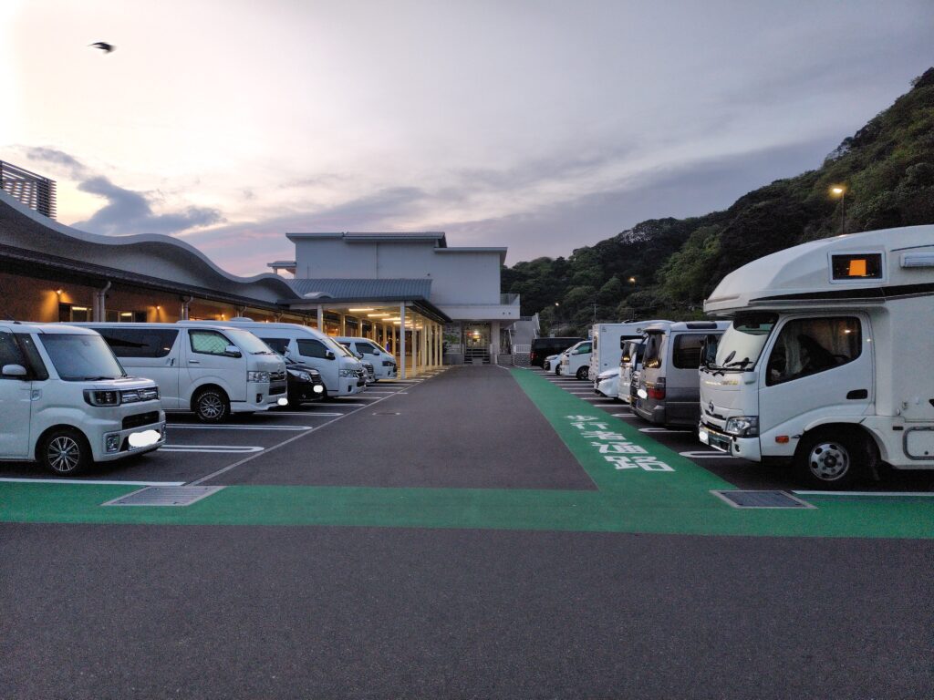 夕暮れの道の駅駐車場に並ぶ車やキャンピングカー。登山前泊の車中泊スポットの様子