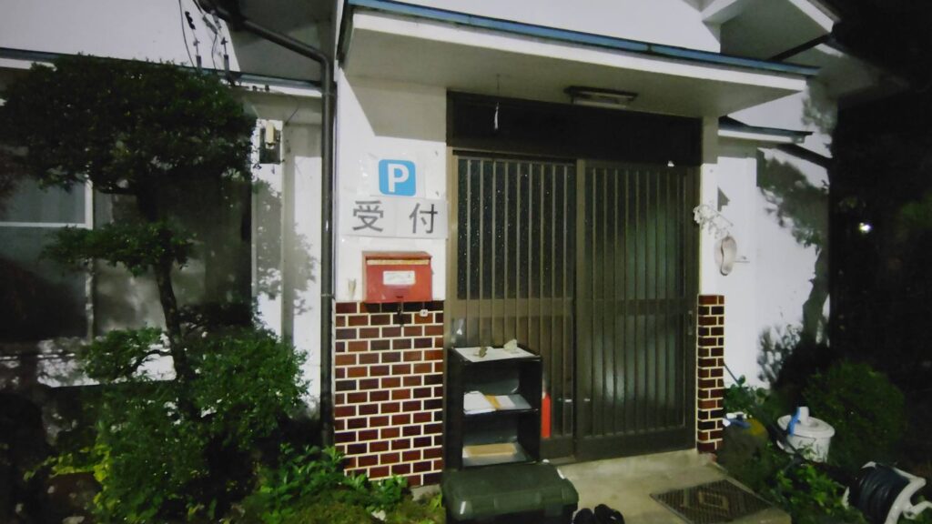 深夜の駐車場受付。玄関前に受付用紙と封筒、ポストが置かれている